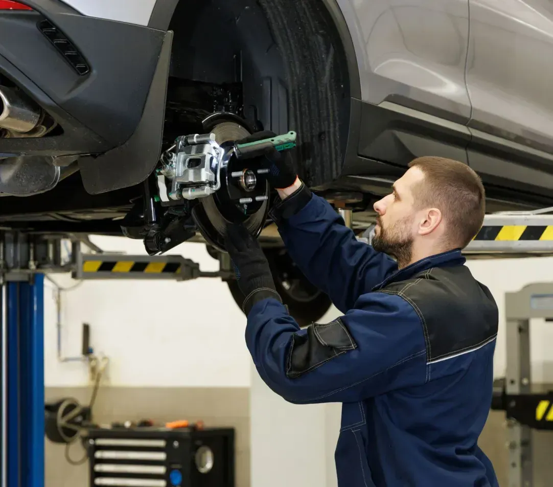 A man is working on a car on a lift in a garage.