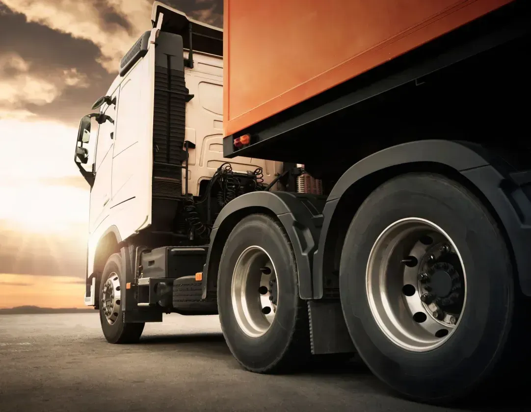 A semi truck is driving down a road at sunset.