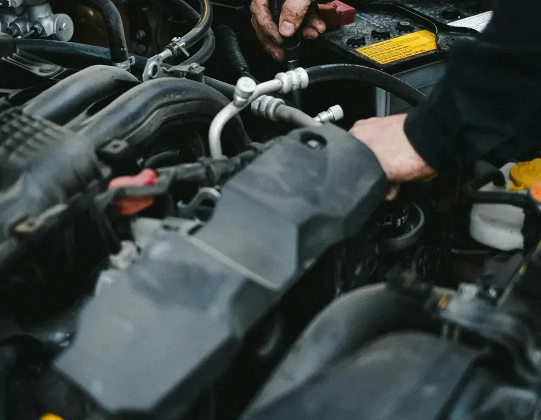A man is working on the engine of a car with a screwdriver.