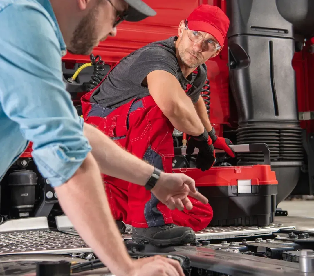 Two men are working on the engine of a truck.
