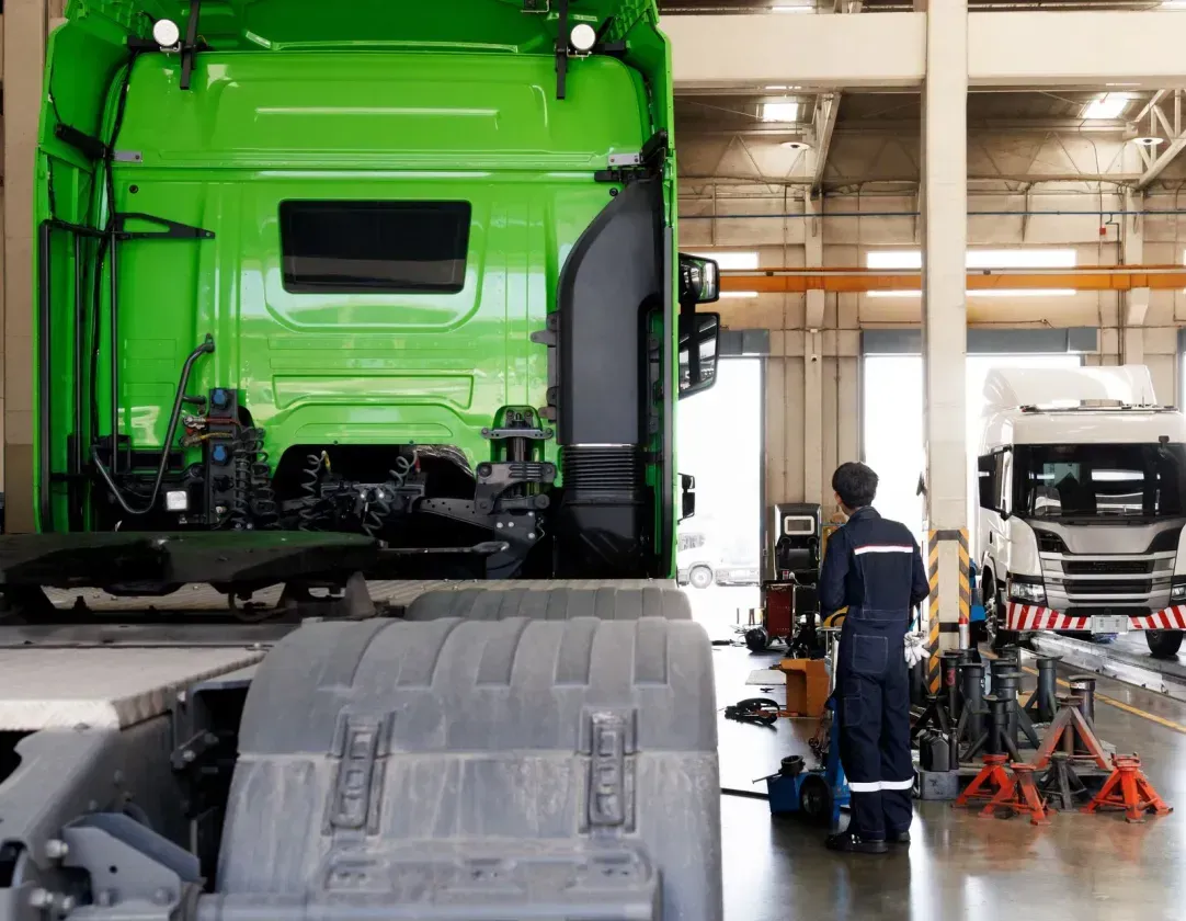 A man is working on a green semi truck in a garage.