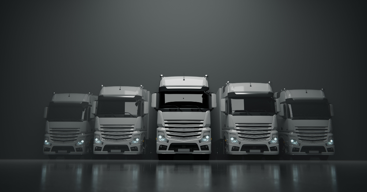 A row of semi trucks are parked next to each other in a dark room.