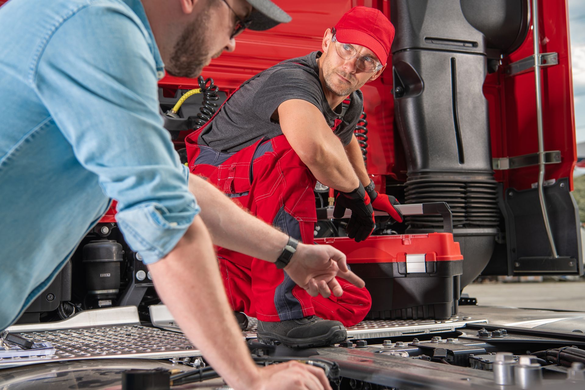 Two men are working on the engine of a truck.