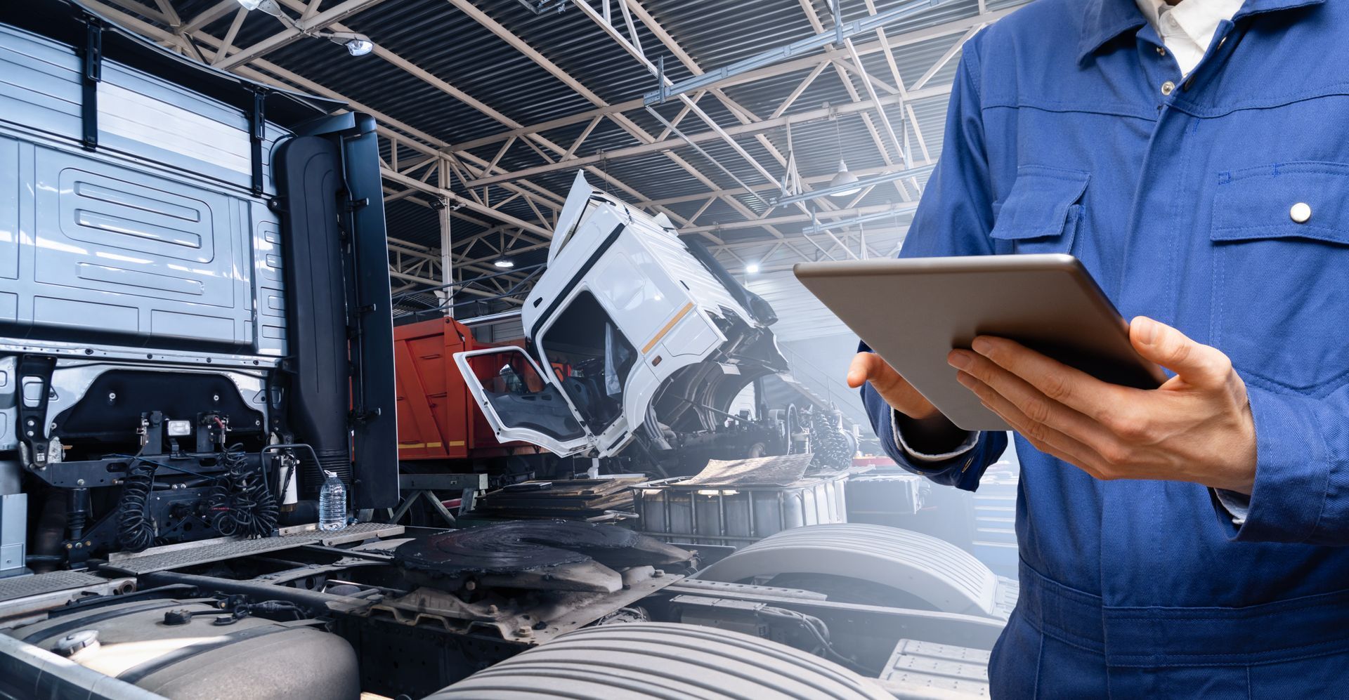 A man is holding a tablet in front of a truck in a warehouse.