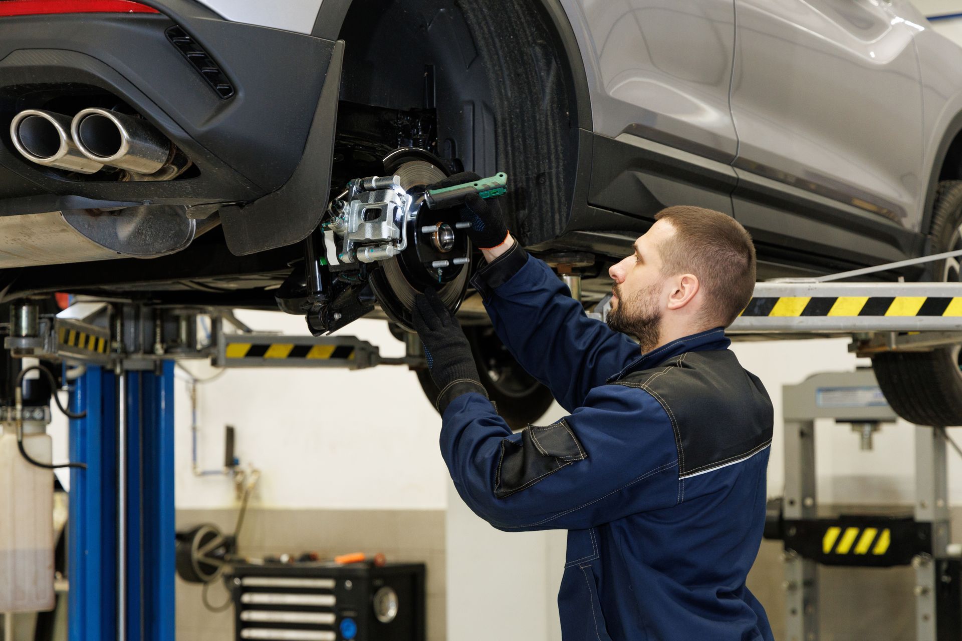 A man is working on a car on a lift in a garage.