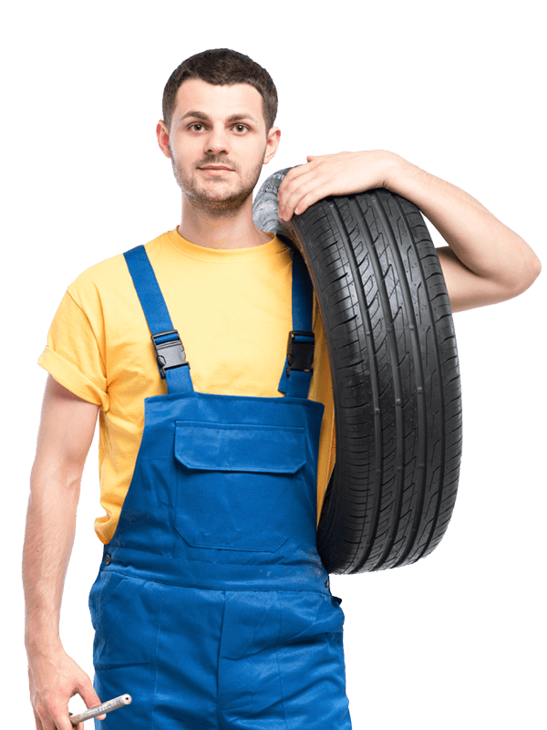 A man in blue overalls is holding a tire and a wrench.