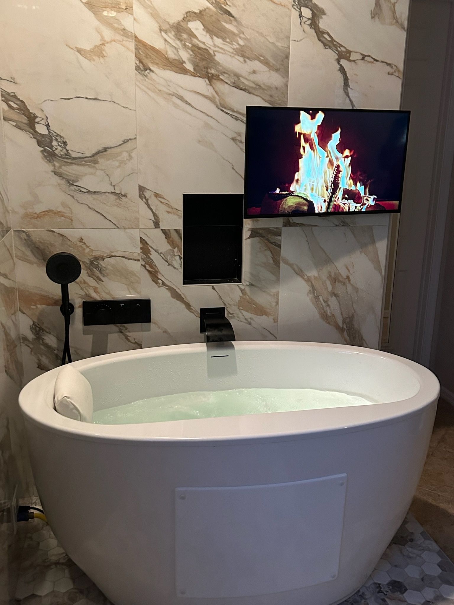 A bathtub in a bathroom with a television on the wall above it.