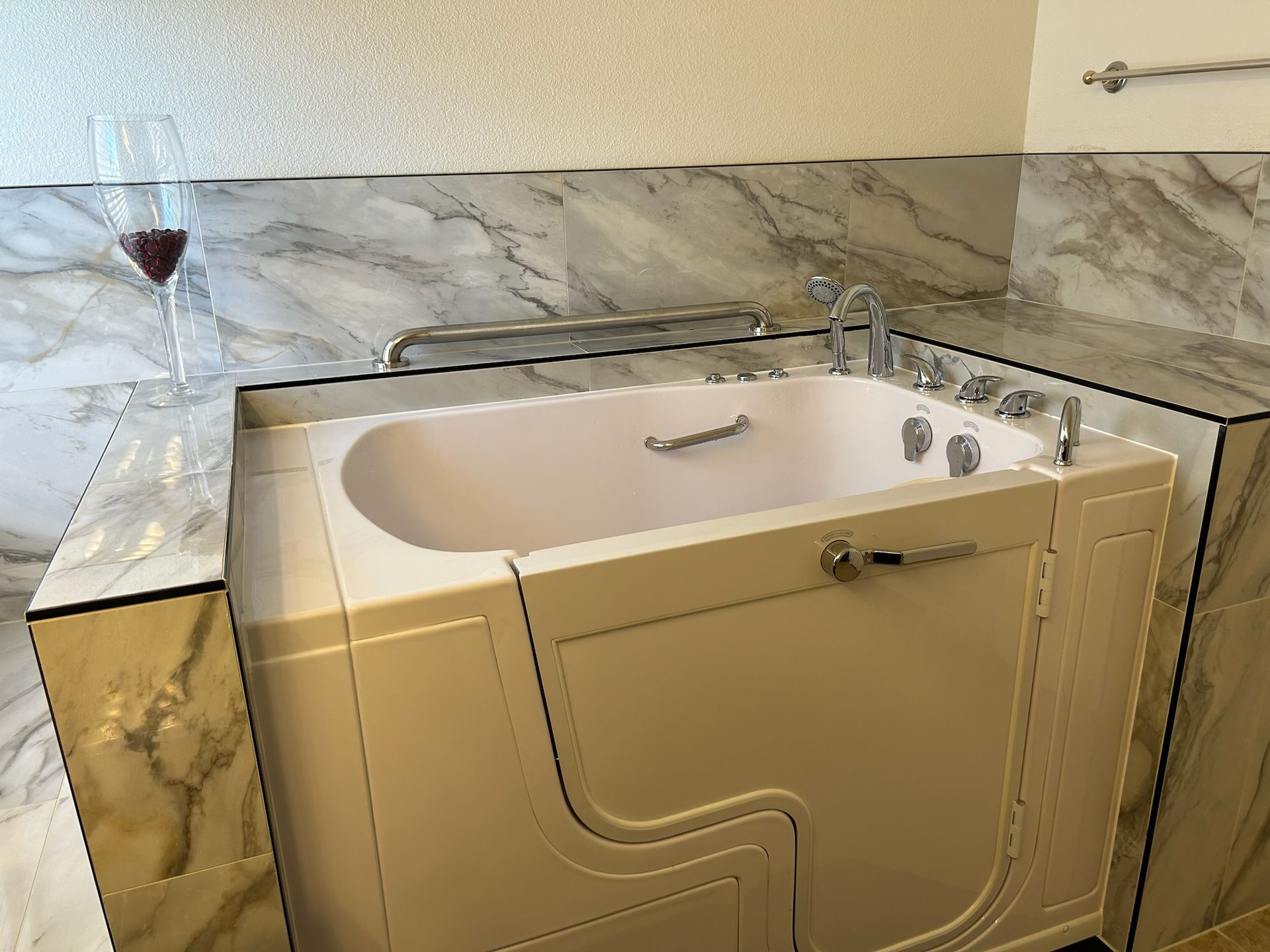 A walk in tub with a glass of wine next to it.