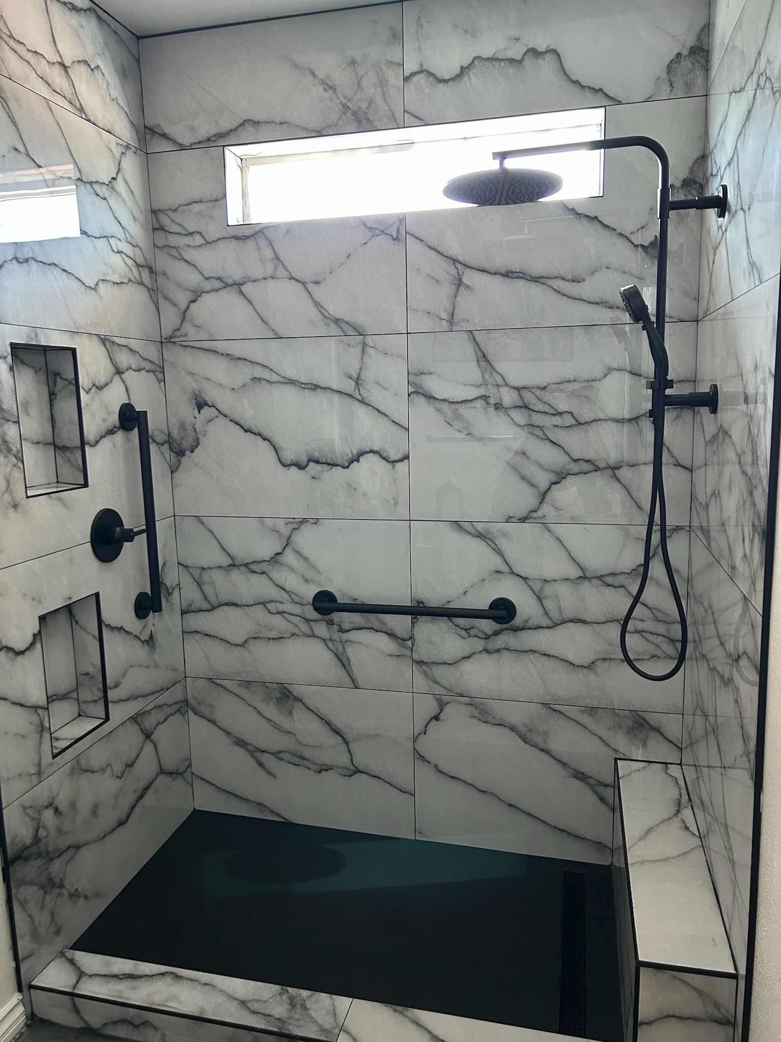 A bathroom with a walk in shower with marble walls and a black shower head.