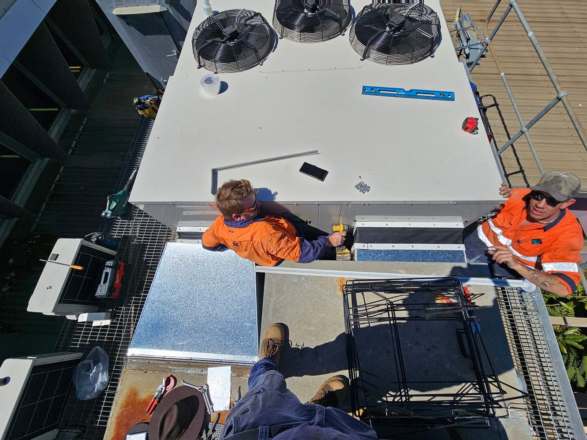 Two Workers in Orange Vests on a Rooftop — Cumming Airconditioning & Sheetmetal in Ryan, QLD