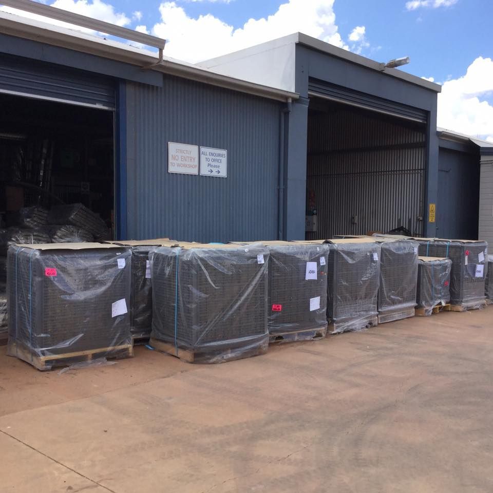 Pallets of Wrapped Items Outside a Blue Industrial Building — Cumming Airconditioning & Sheetmetal in Ryan, QLD