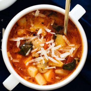 White bowl of vegetable soup with grated cheese, gold spoon on a dark blue background.