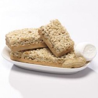 Three peanut butter crumble bars on a white plate with a scoop of white icing and a peanut.