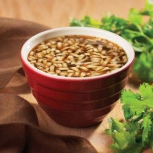 Red bowl of soup with pasta, surrounded by cilantro.