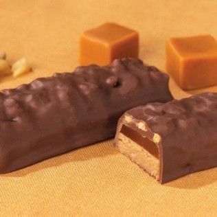 Chocolate-covered candy bar, cut to show layers of caramel and nougat, with caramel squares on orange surface.