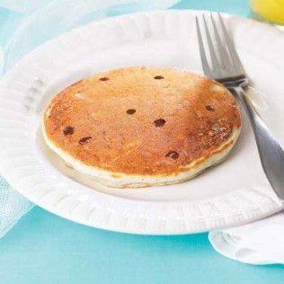 Chocolate chip pancake on a white plate with a fork, set on a blue surface.