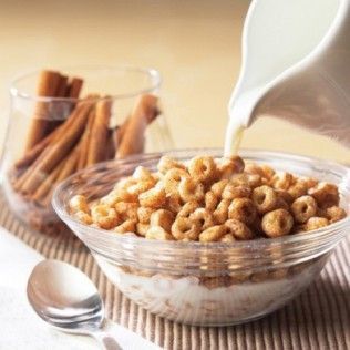 Bowl of cinnamon cereal being poured with milk. Jar of cinnamon sticks in the background.