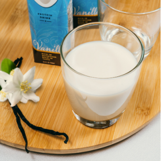 Glass of vanilla protein drink on wooden board, with flower and vanilla bean.