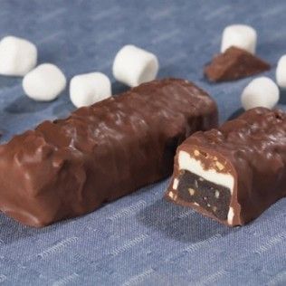 Chocolate-covered candy bars with marshmallow filling and scattered marshmallows on blue cloth. One bar is cut.