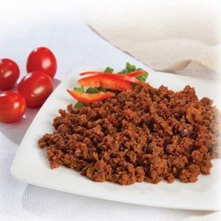 Ground meat seasoned with red spices on a white plate, tomatoes in background.