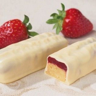 Two white-chocolate-covered bars with a strawberry filling next to fresh strawberries on a white cloth.