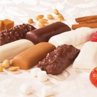 Assorted candy bars, peanuts, marshmallows, cinnamon sticks, and strawberries on a patterned surface.