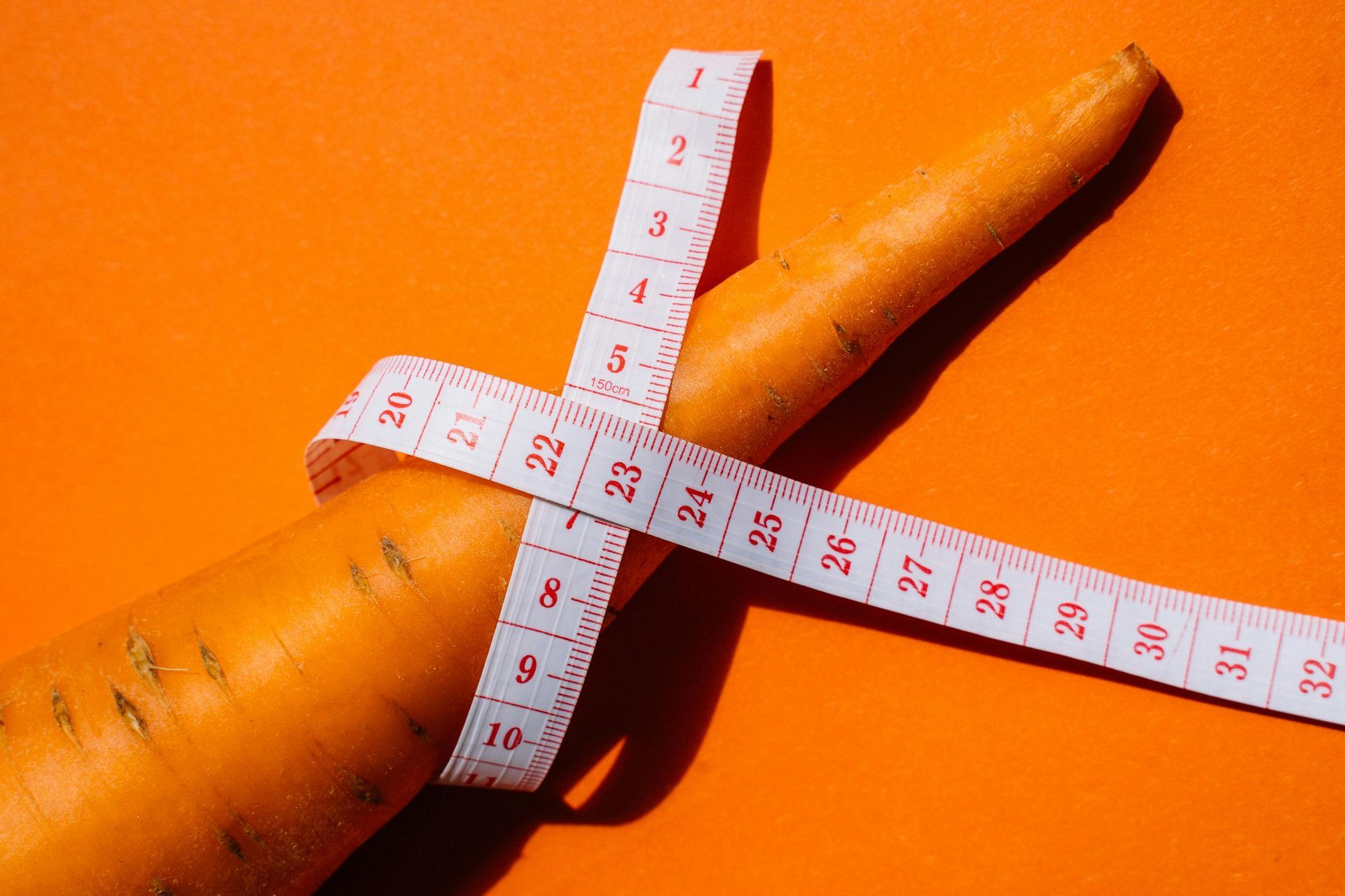 Orange carrot wrapped with white measuring tape, orange background.