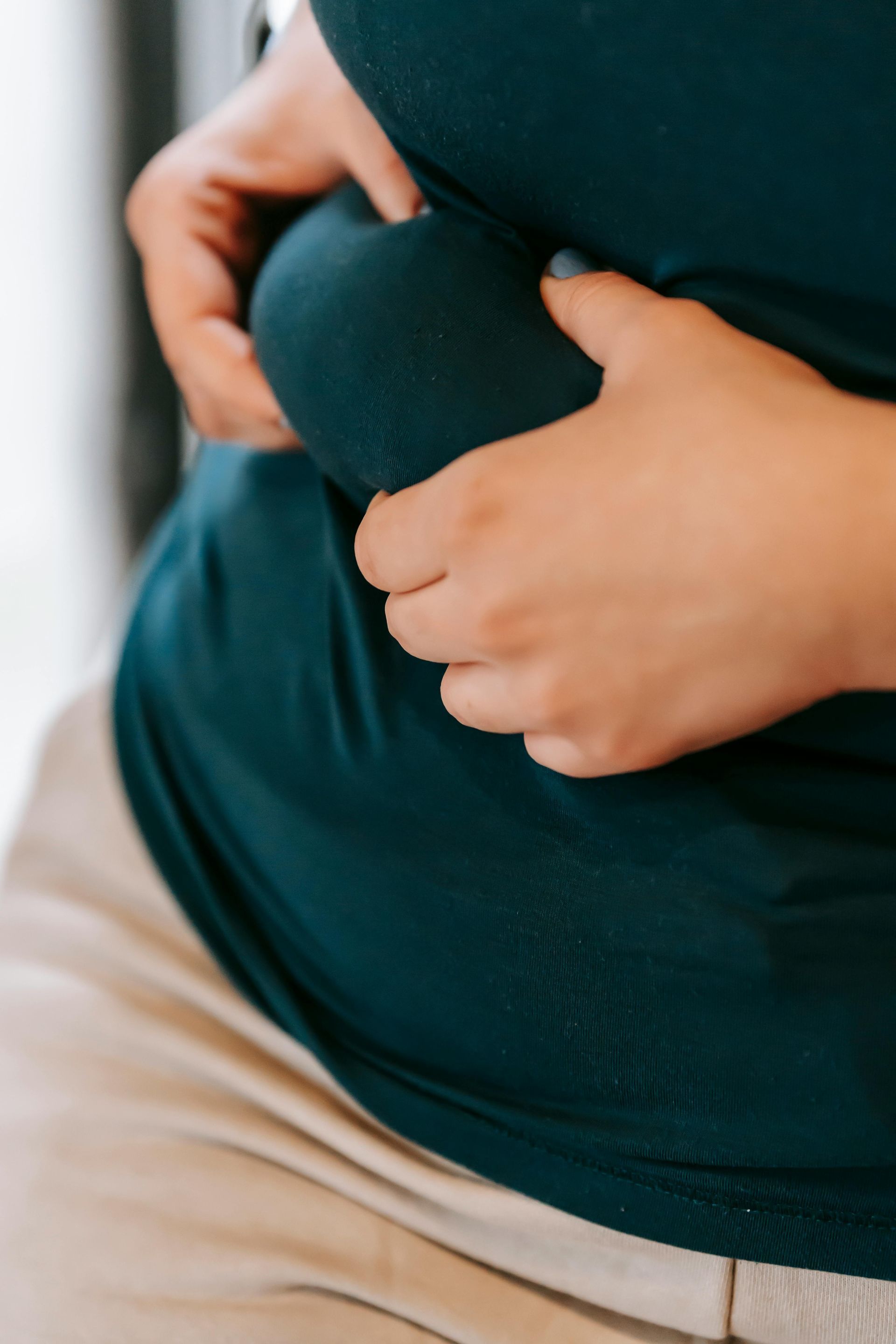 Person pinching abdominal fat through a dark blue shirt.