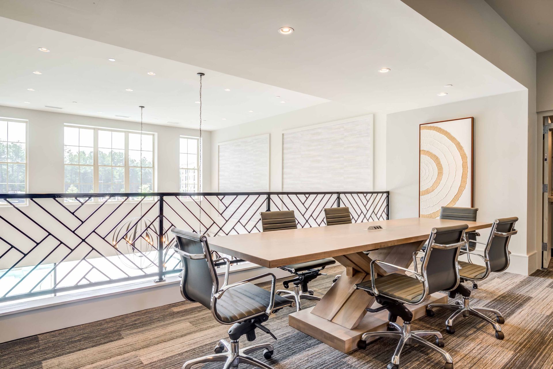 Conference room with long table, black rolling chairs, decorative railing, and modern art.