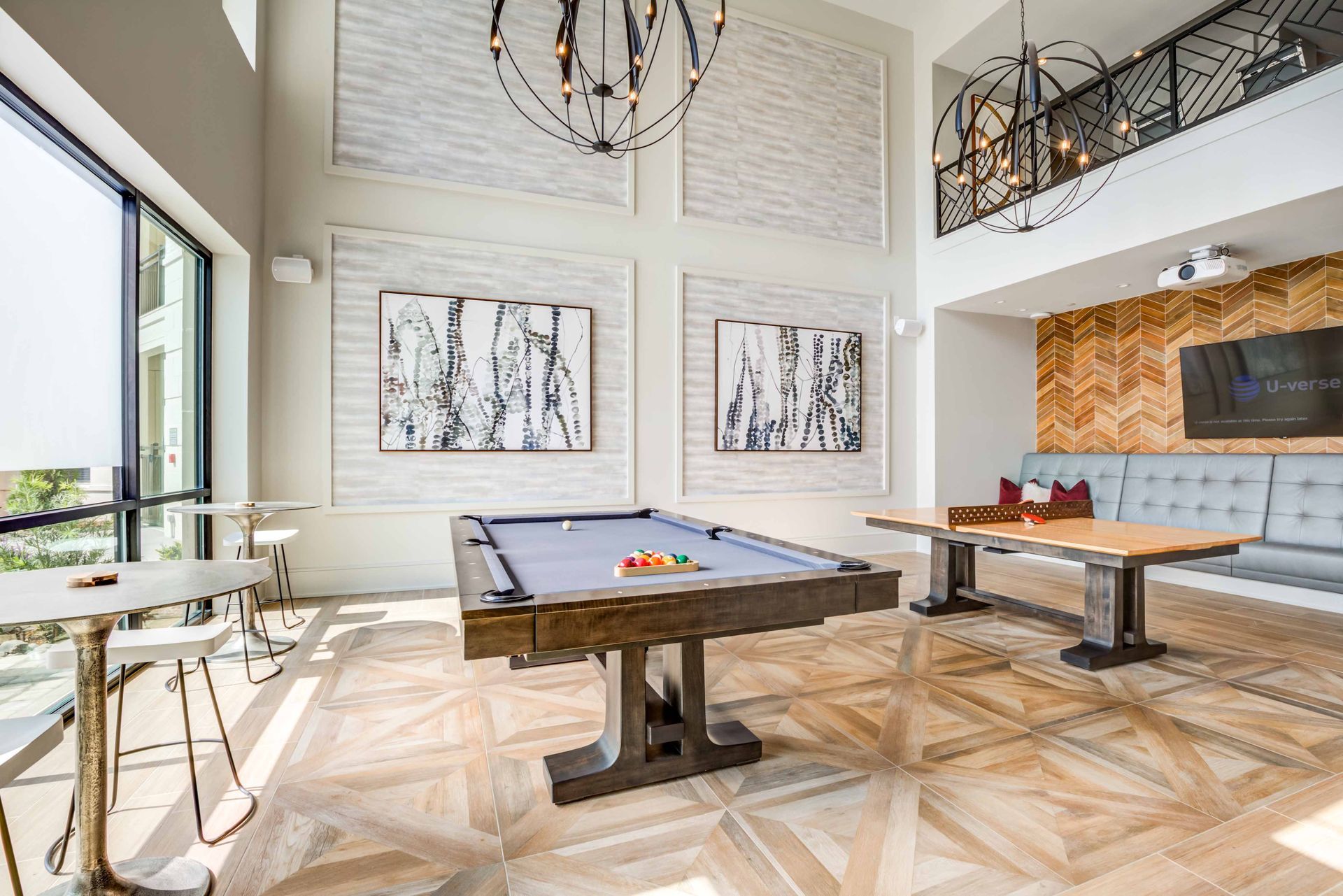 A bright, modern game room with a pool table, lounge area, and a large window.