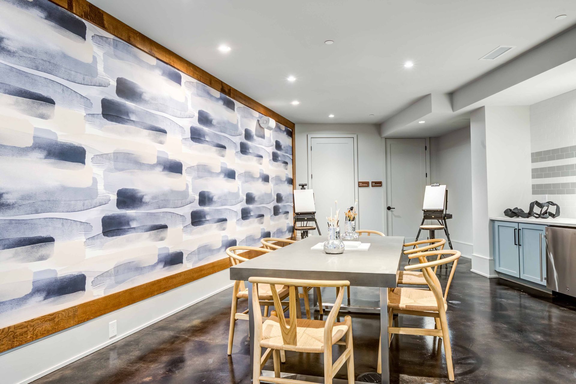 Dining room with long table, watercolor wall, chairs, easels, and mini-fridge.