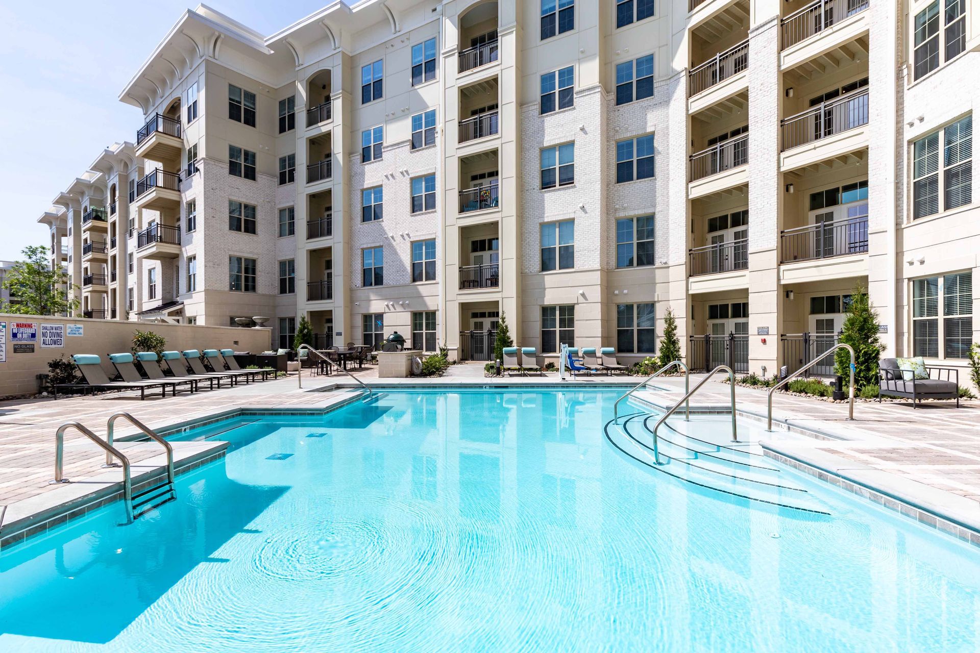 Swimming pool in front of an apartment building with several balconies and a bright, sunny day.