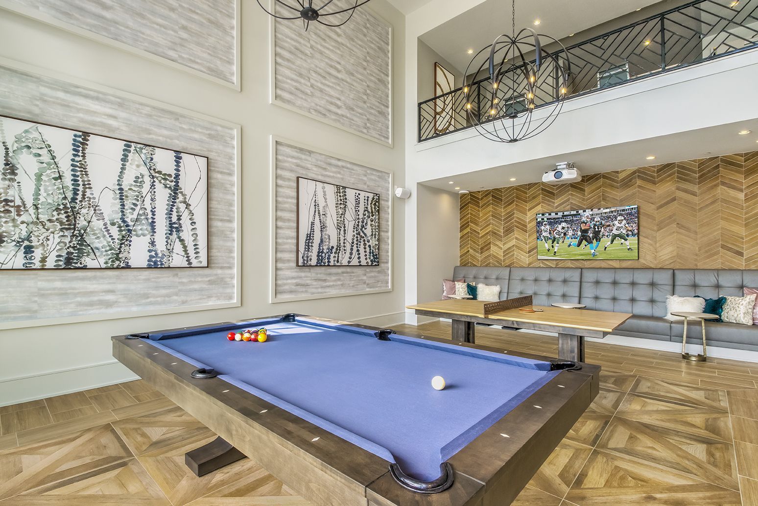 Lounge room with fireplace, white walls, and a large stadium painting. Beige sofa with turquoise pillows.