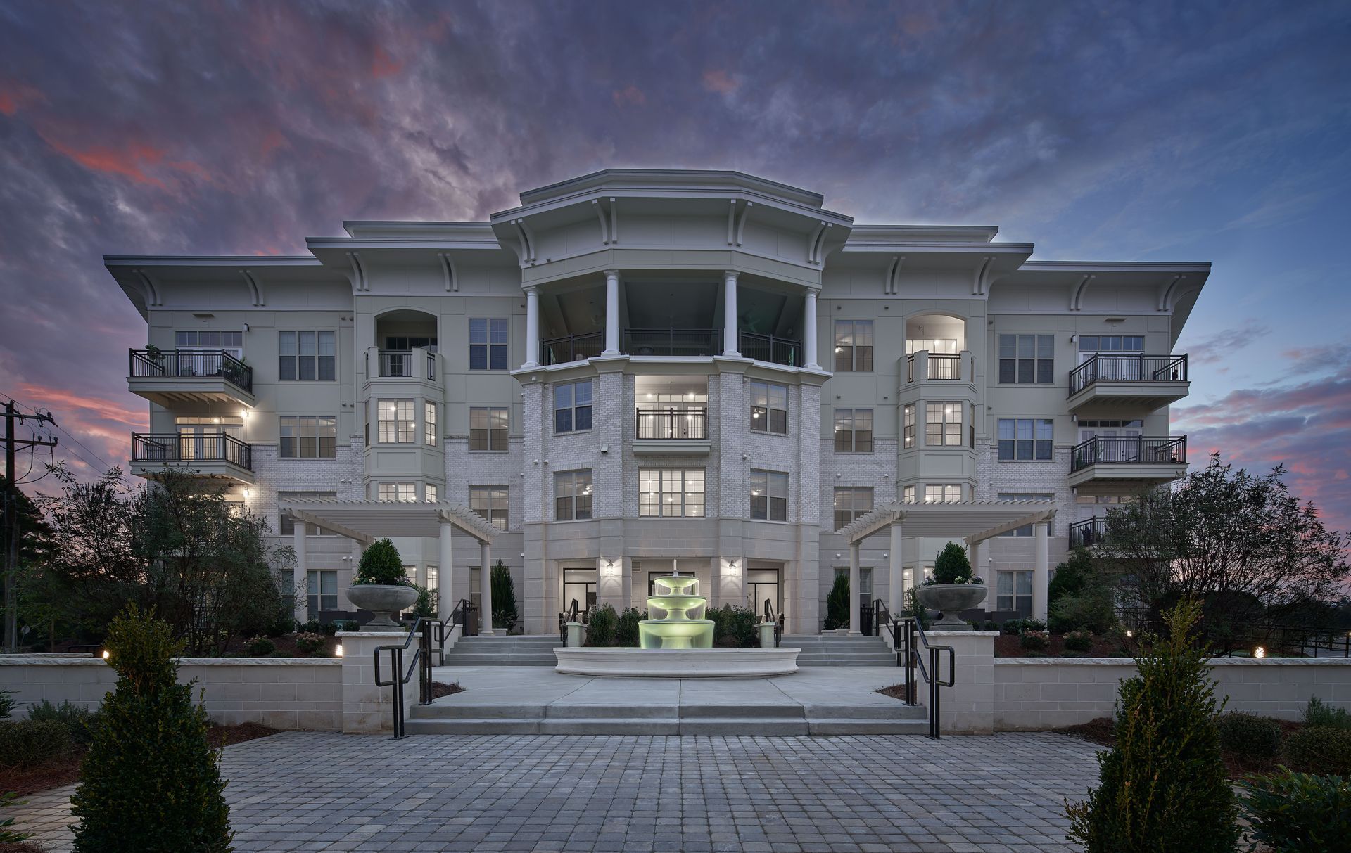 Swimming pool with stairs, surrounded by a building with balconies. Blue water, gray concrete.