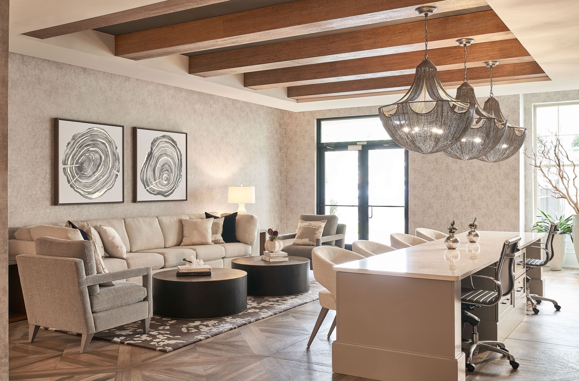Lounge room with neutral tones, beige sofa, dark wood beams, chandelier, and a white countertop island.