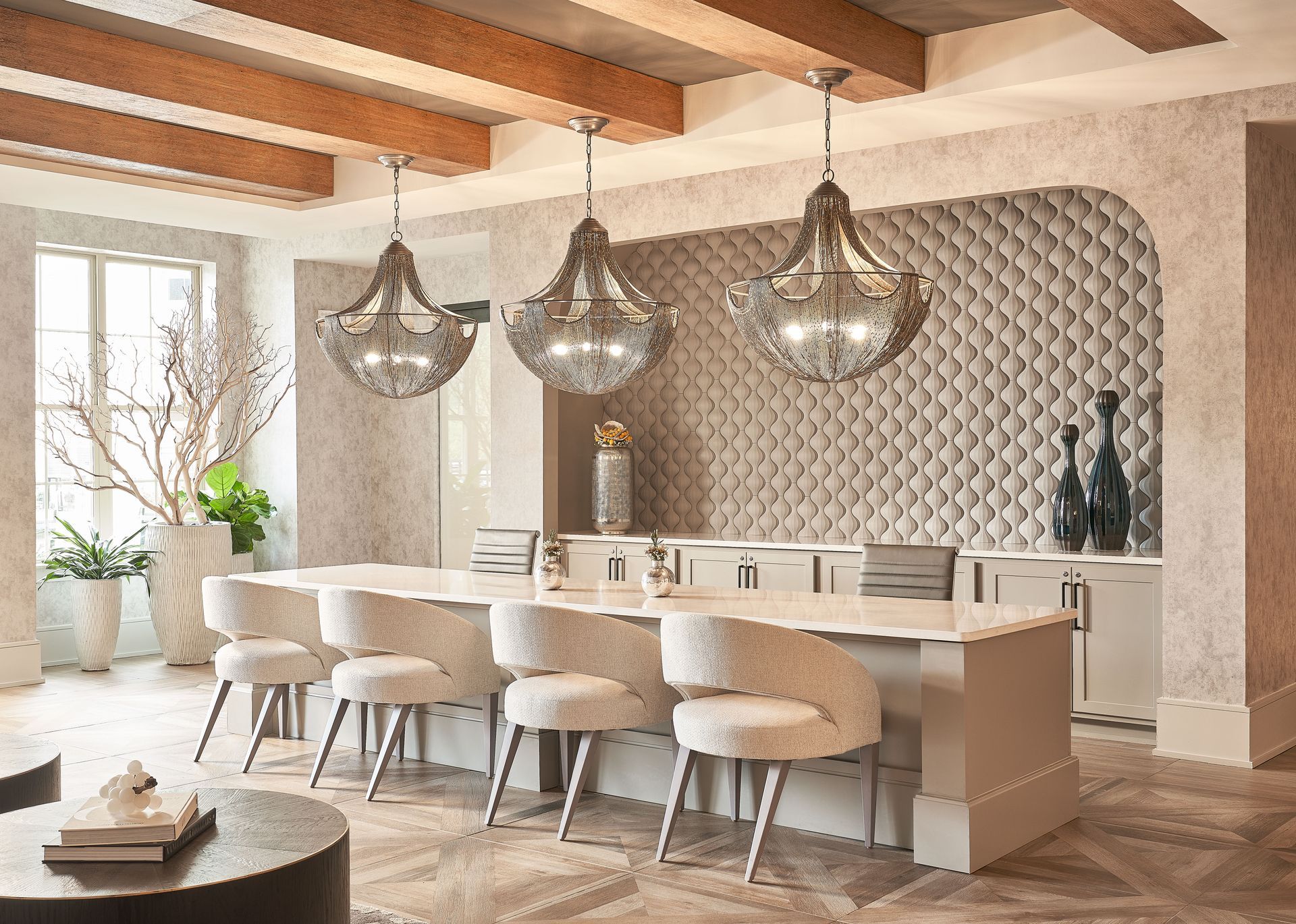 Luxurious clubhouse kitchen with three chandeliers over a long island with seating, textured wall.
