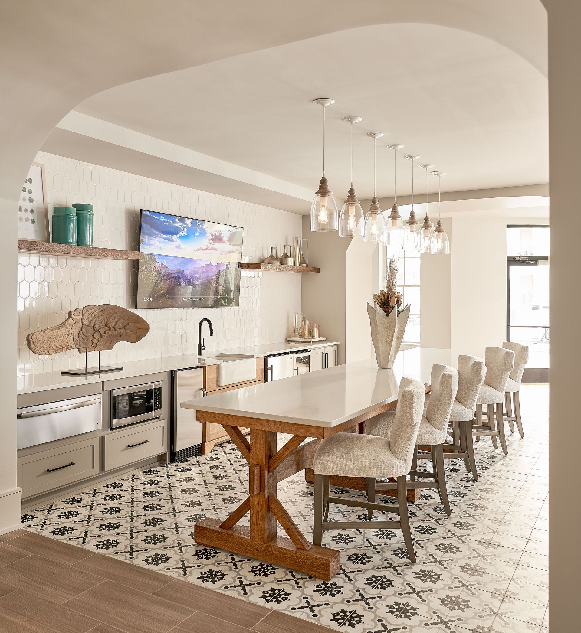 Clubhouse kitchen with white countertops, wooden table, patterned floor, and bar stools.