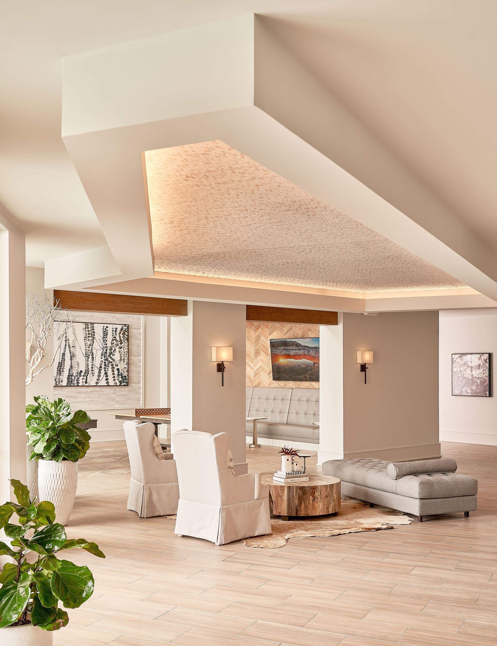 Spacious, modern lounge area with white walls, textured ceiling, and neutral-toned furniture; art and plants.