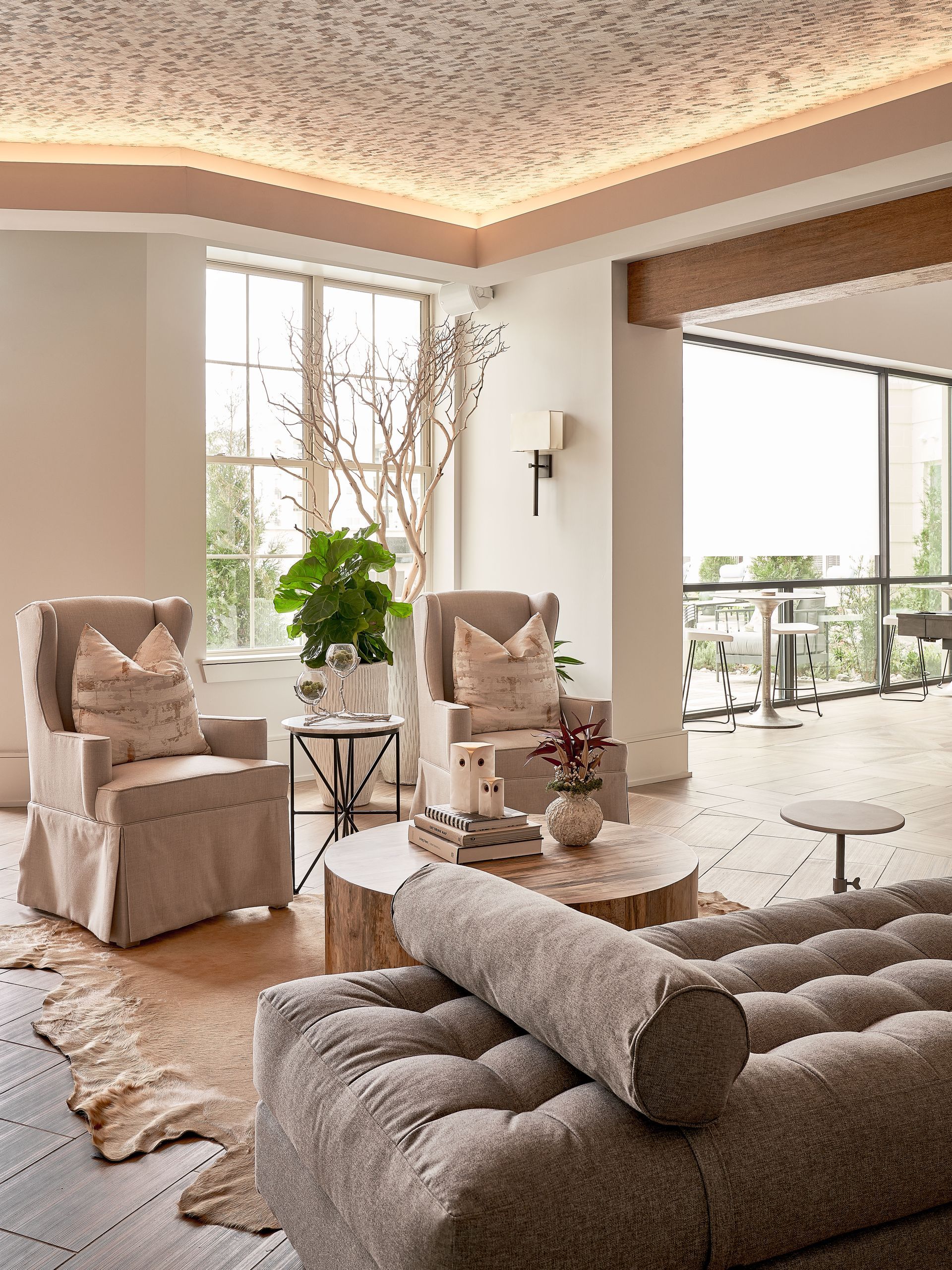 Lounge room with neutral tones, two armchairs, a couch, a tree trunk coffee table, and large windows.