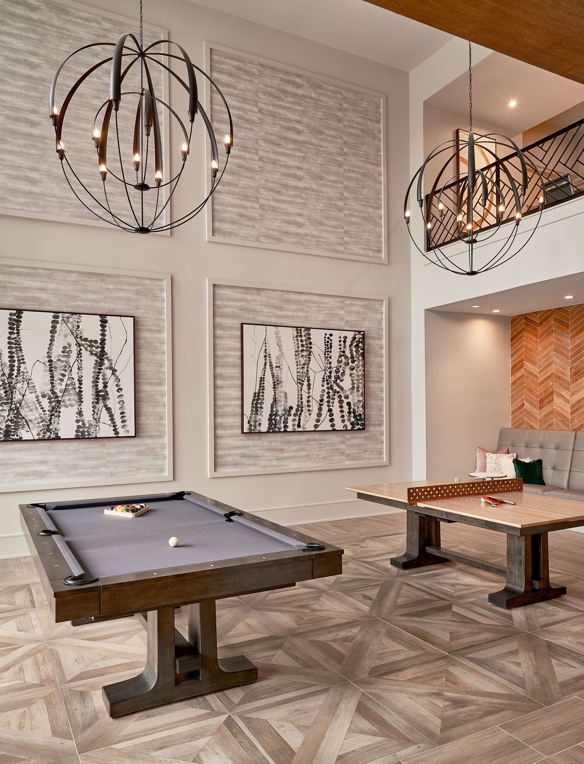 Game room with pool and ping pong tables, art, and two spherical chandeliers.