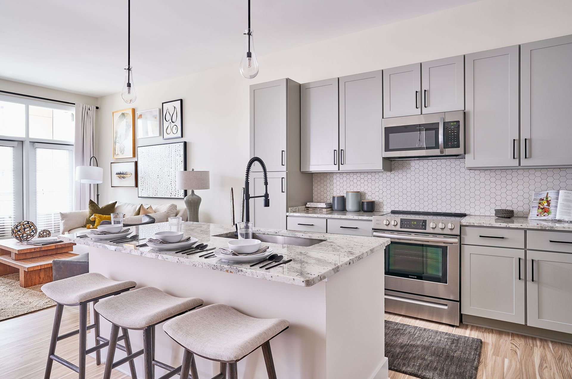 Modern kitchen with island, stainless steel appliances, and gray cabinets. Open to a living room with sofa.