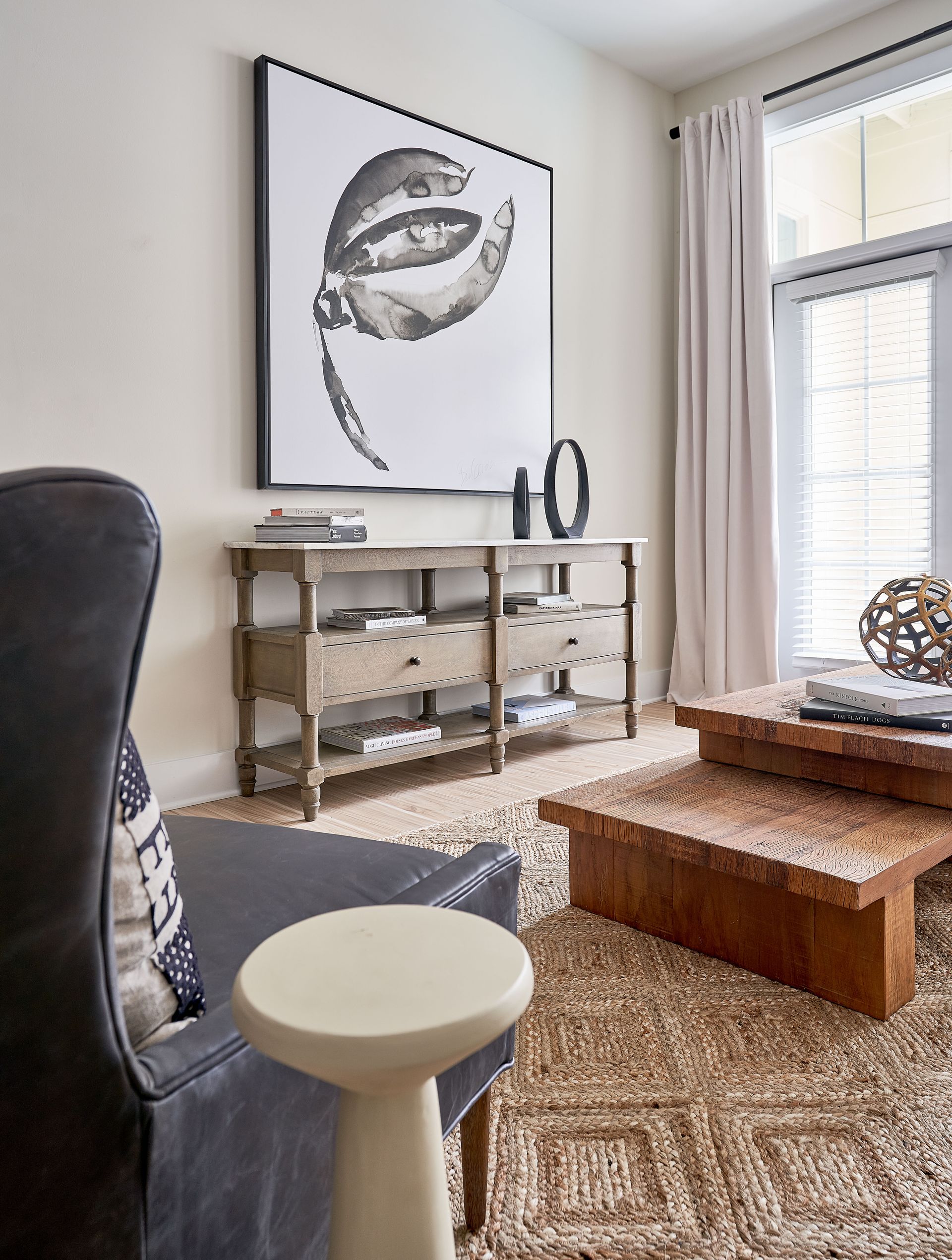 Lounge room with artwork, console table, arm chair, wood tables, and window.