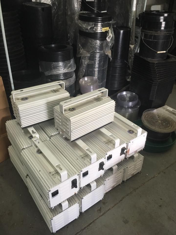 A stack of white plastic containers with handles, in a storage area with black plastic pots and containers.