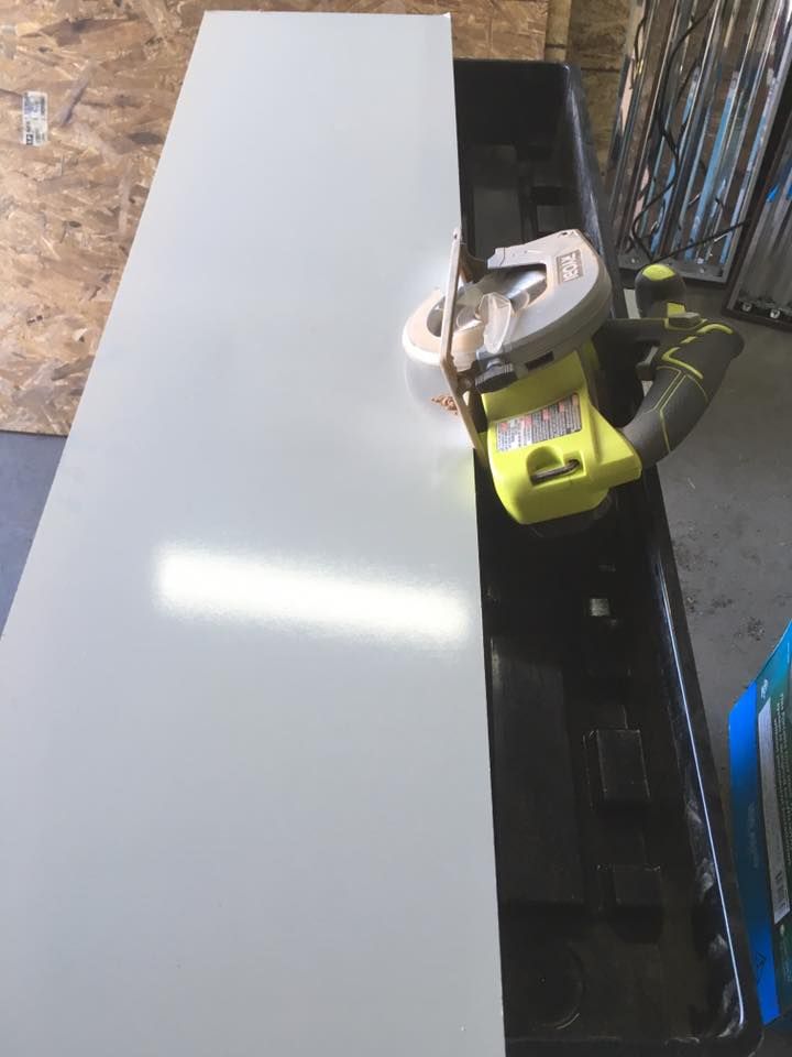 A person cutting a long, gray sheet of metal with a circular saw. Black container underneath.