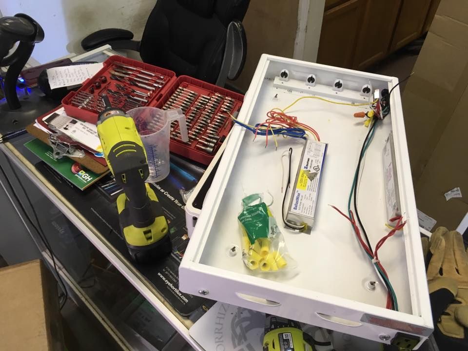 Open white electrical box with wires and components, tools on a cluttered workbench.
