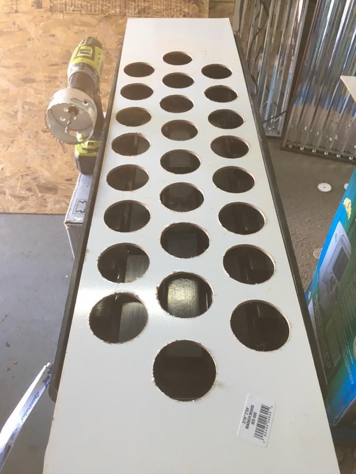 White rectangular board with evenly spaced circular holes, a power drill is nearby.