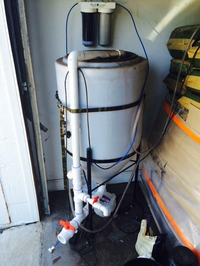 Water filtration system with white tank, filters, and pipes in a garage.