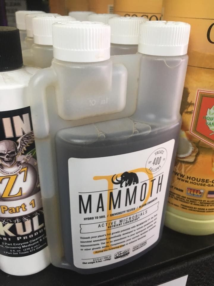 Bottle of MAMMOTH plant additive with white label and elephant logo, displayed on a shelf.