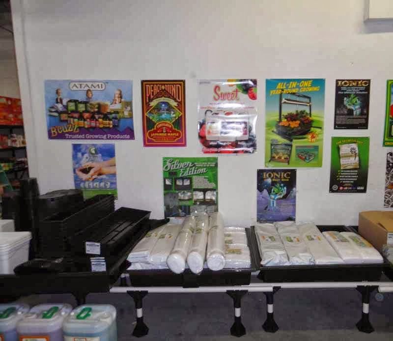 Indoor display of gardening supplies, posters on wall above, products on tables.