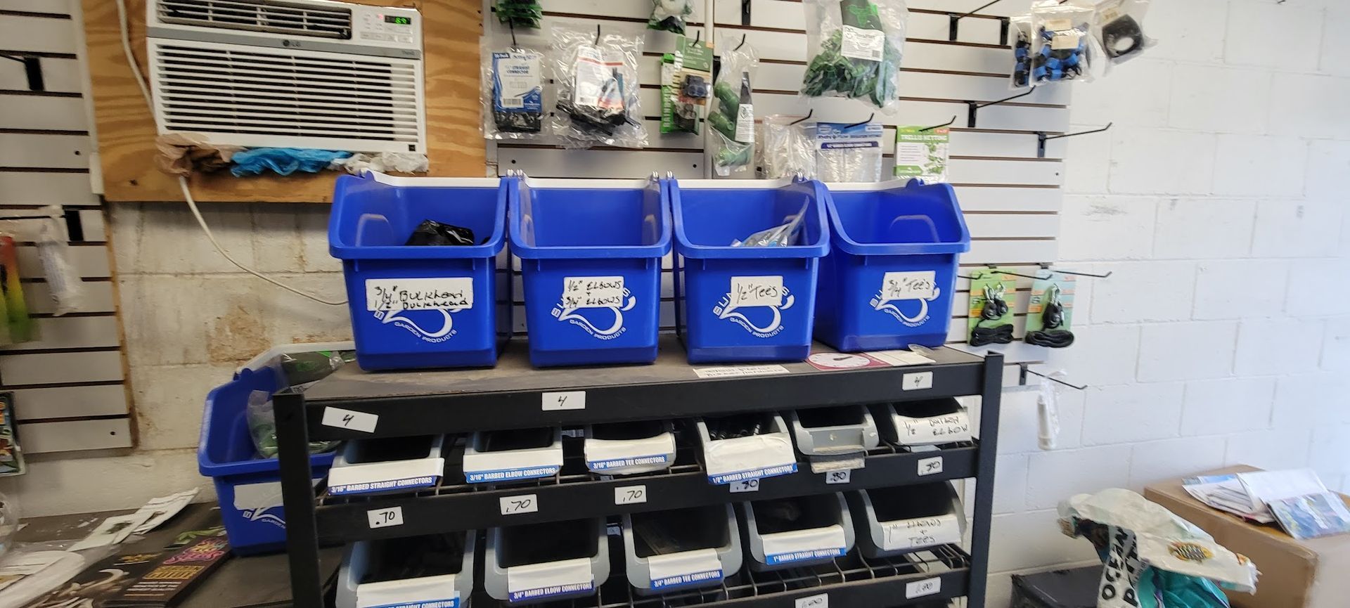 Blue bins on a shelf in a store, below bins are more shelves filled with containers, shelves are against a white-slat wall.